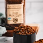 Close-up of India Tree Dark Muscovado Sugar, a rich unrefined brown sugar, in a measuring cup, with its retail bag softly in the background.
