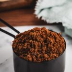 Close-up of India Tree Dark Muscovado Sugar, a rich, unrefined brown sugar, filling a clear measuring cup.