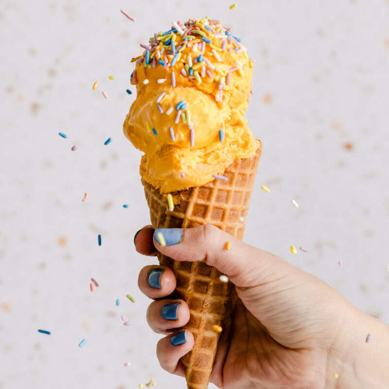 Natural Pastel Rainbow Sprinkles from India Tree Nature's Colors Carnival collection cascading onto a scoops of ice cream in a waffle cone, creating a festive treat.