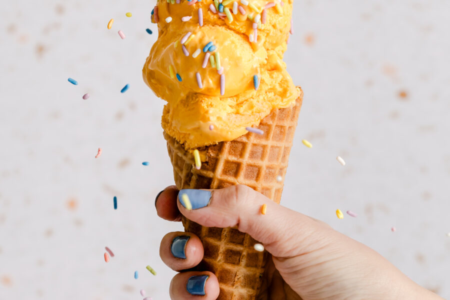 Natural Pastel Rainbow Sprinkles from India Tree Nature's Colors Carnival collection cascading onto a scoops of ice cream in a waffle cone, creating a festive treat.