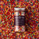 Overhead shot of India Tree Natural Rainbow Sprinkles in a jar on a vibrant bed of colorful sprinkles